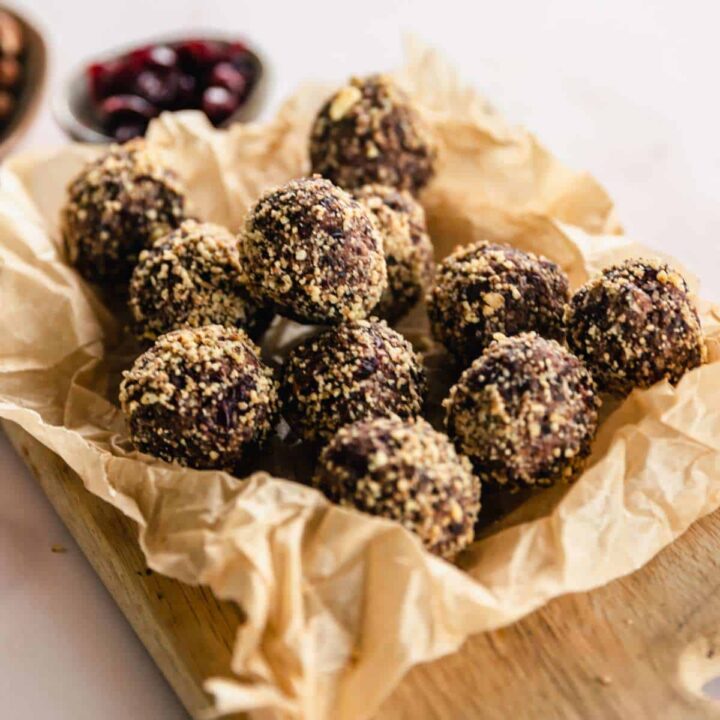 Cranberry and Dark Chocolate Bliss Balls stacked on a wooden chopping board on a marble bench top.