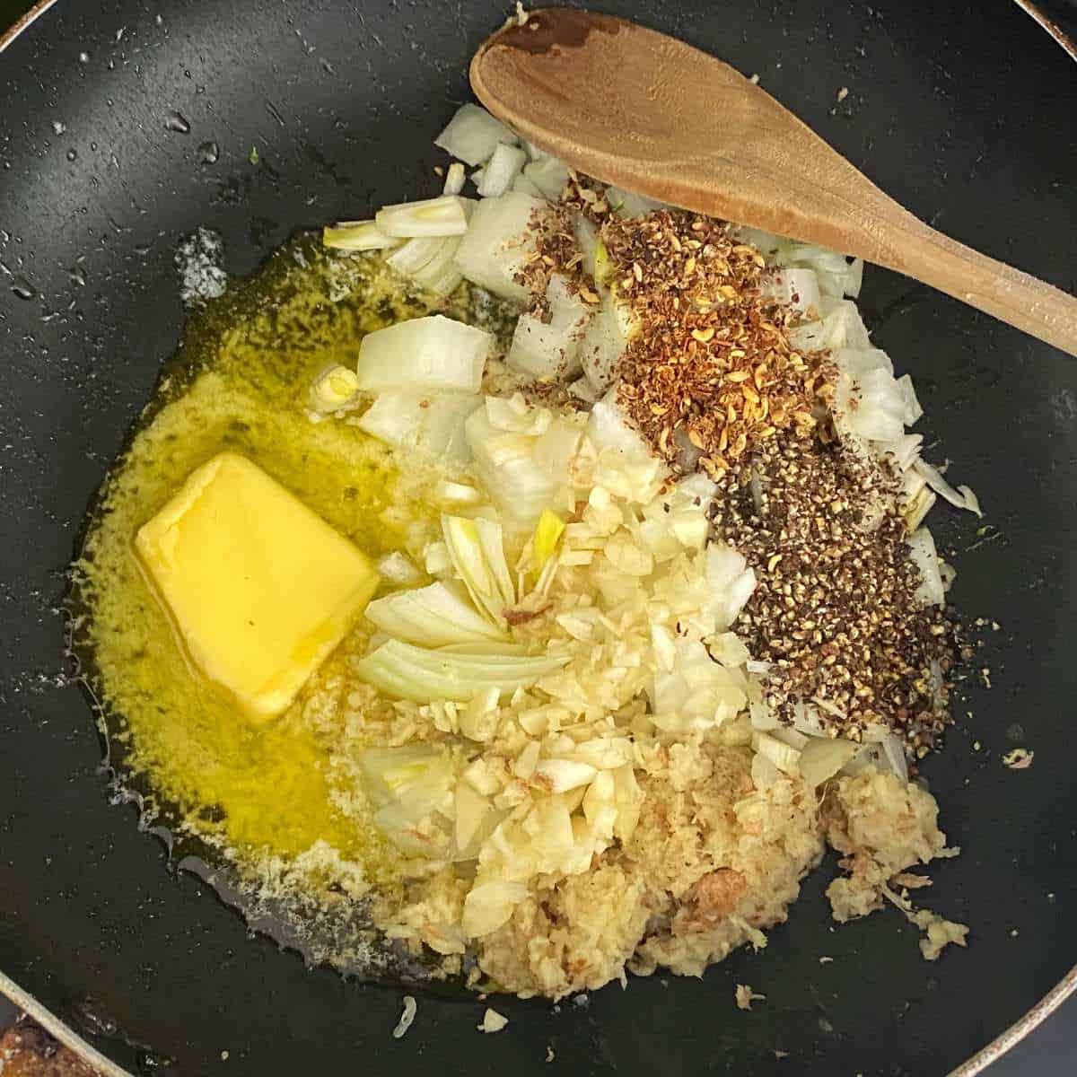 Melted butter, sliced onion, garlic and ginger as well as other ingredients for the Black Pepper Tofu simmering over a low heat in a fry pan.