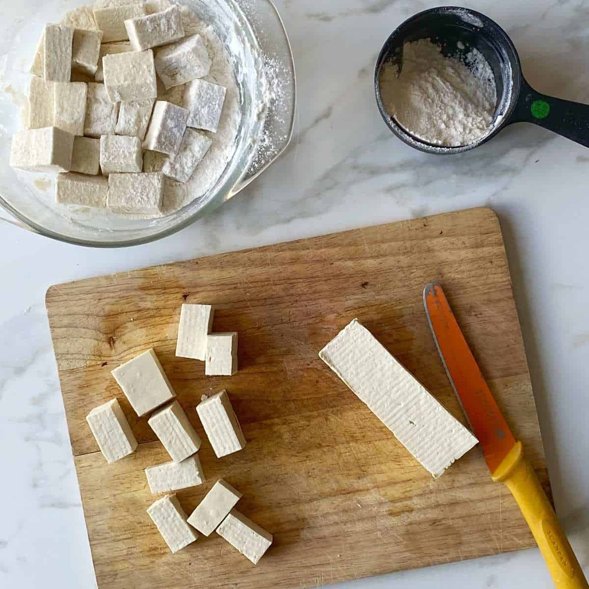 Cubed tofu being tossed through flour to help gently fry and crisp in a medium frypan.