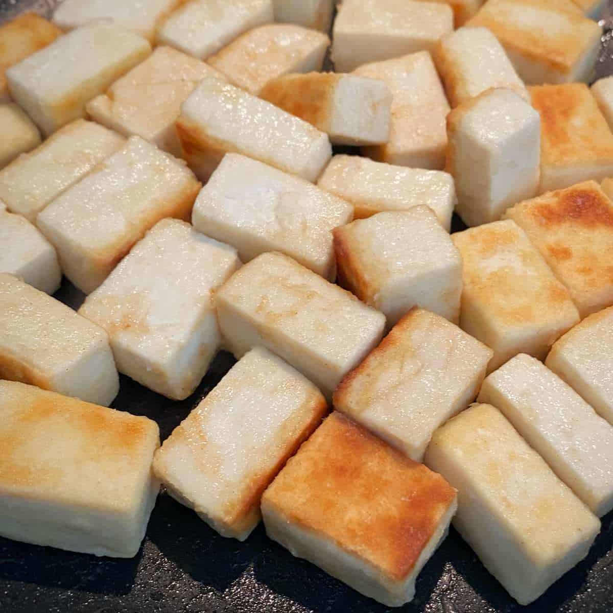 Cubes of tofu gently toasted in a fry pan.