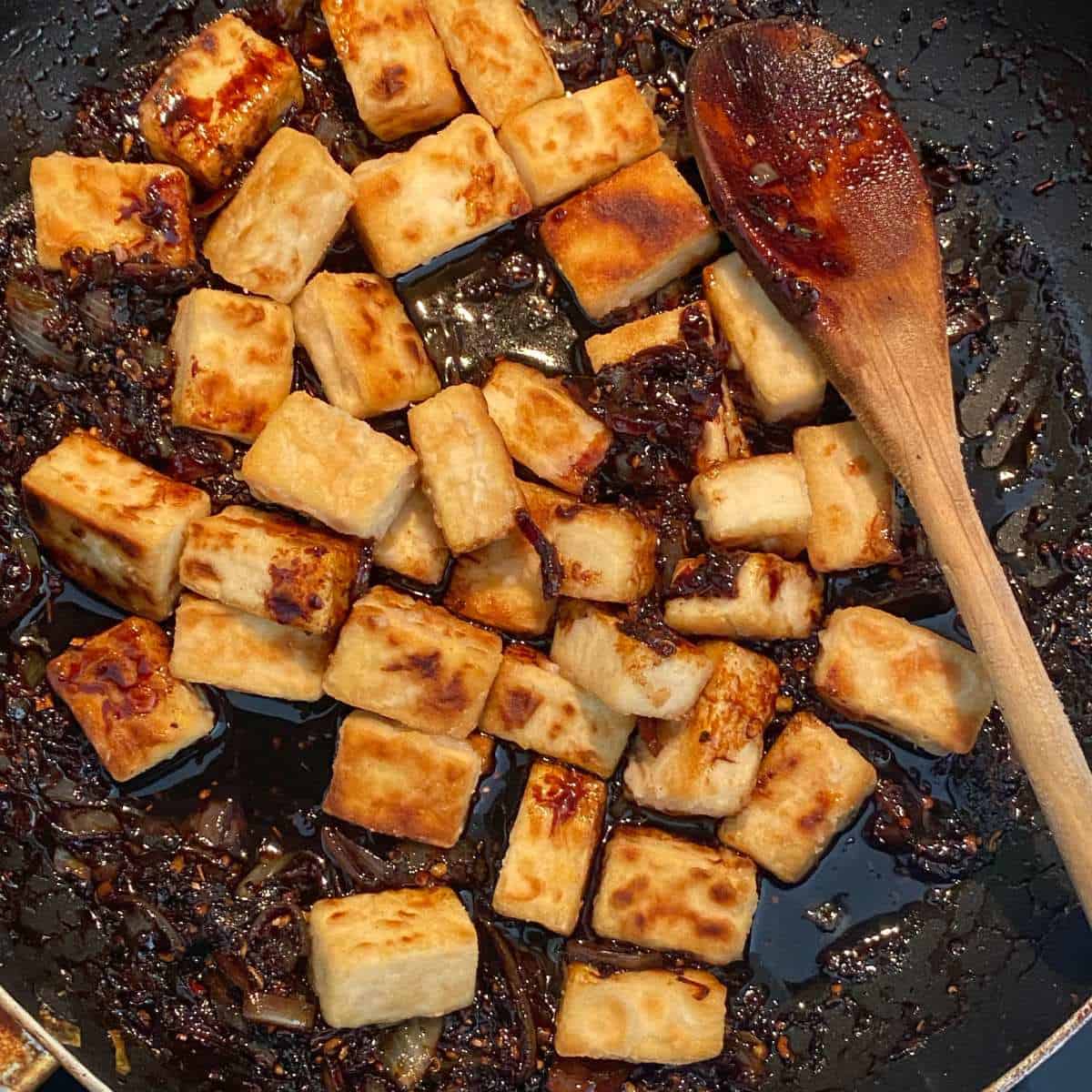 Cooked cubed of tofu being added to the black pepper marinade for Black Pepper Tofu