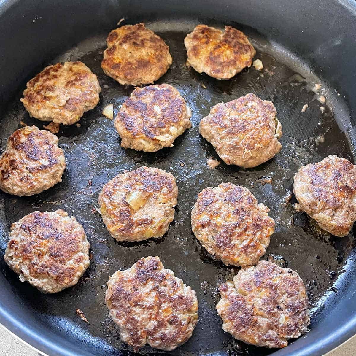 The small burger patties frying in a medium sized frypan to make Cheeseburger Sliders.