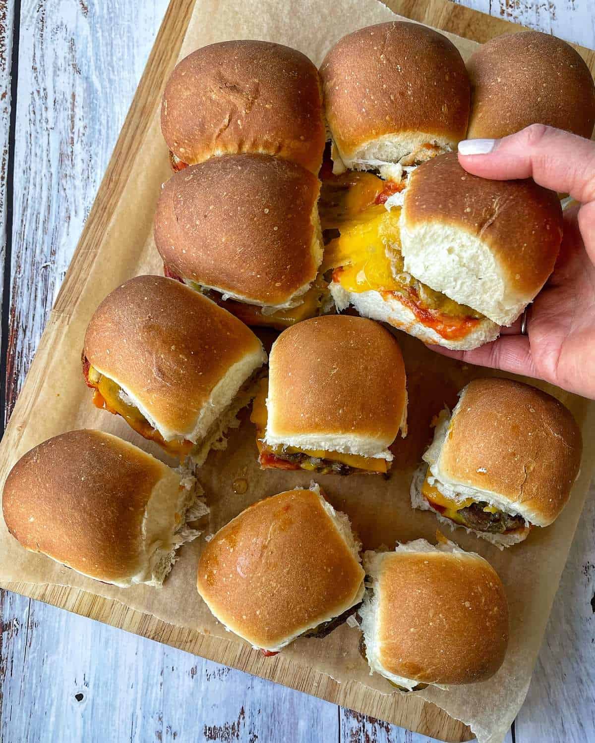 A birds eye view shot of the cooked Cheeseburger Sliders with one burger being lifted to show the melted cheese.