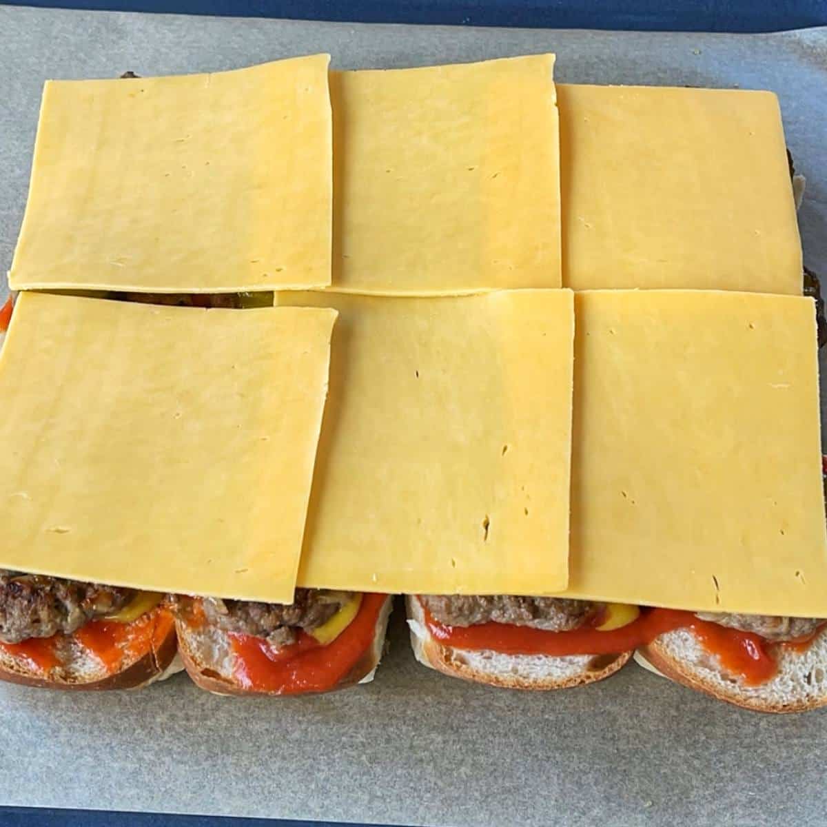 A shot of sliced buns with sauces, patties and cheese slices showing the process of how the Cheeseburger Sliders are assembled together.