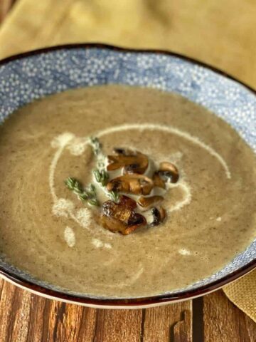 Creamy Mushroom Soup served in a blue soup bowl with a few fried mushrooms and sprig of thyme.