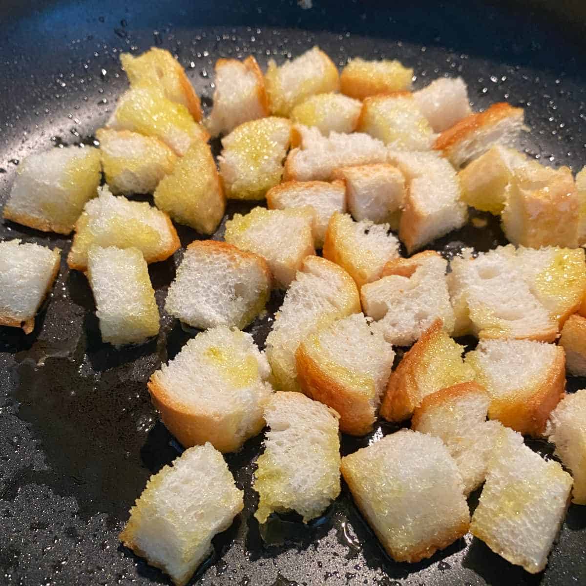 Small cubes of bread frying lighting in a fry pan to make croutons for Leak and Potato Soup.