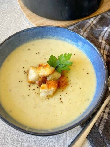 Leak and Potato Soup severed in a blue soup bowl with a few croutons and sprig of parsley on top.
