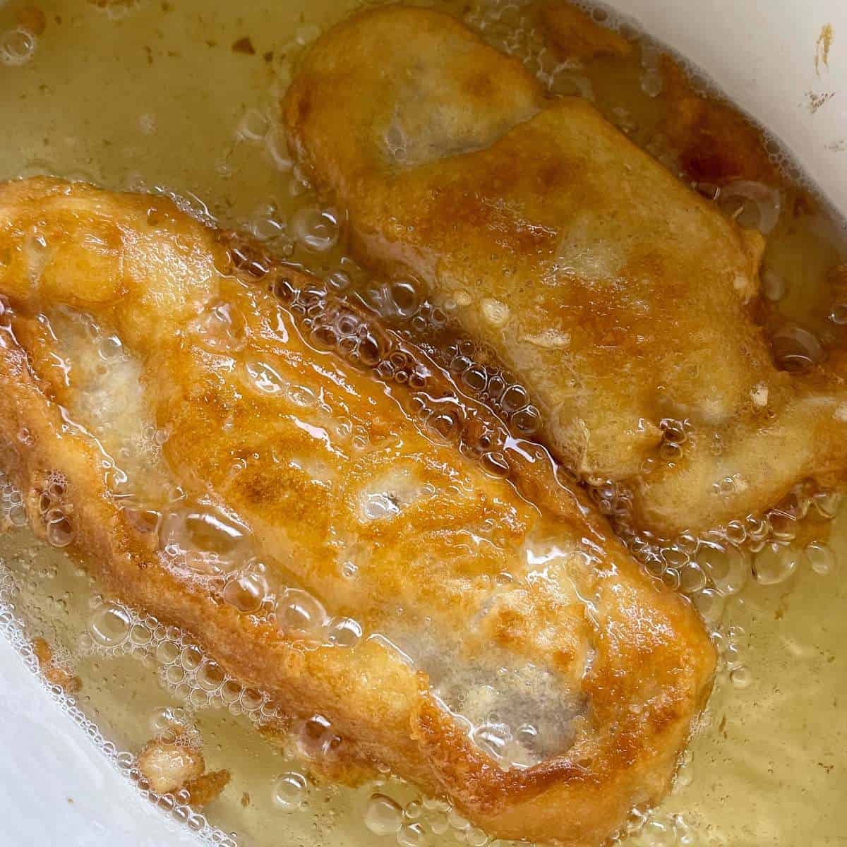 Two pieces of battered fished being gently fried in oil.