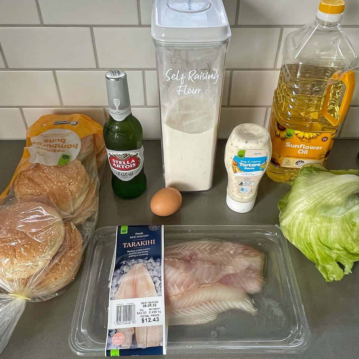 The ingredients for battered fish burgers on a grey bench top.