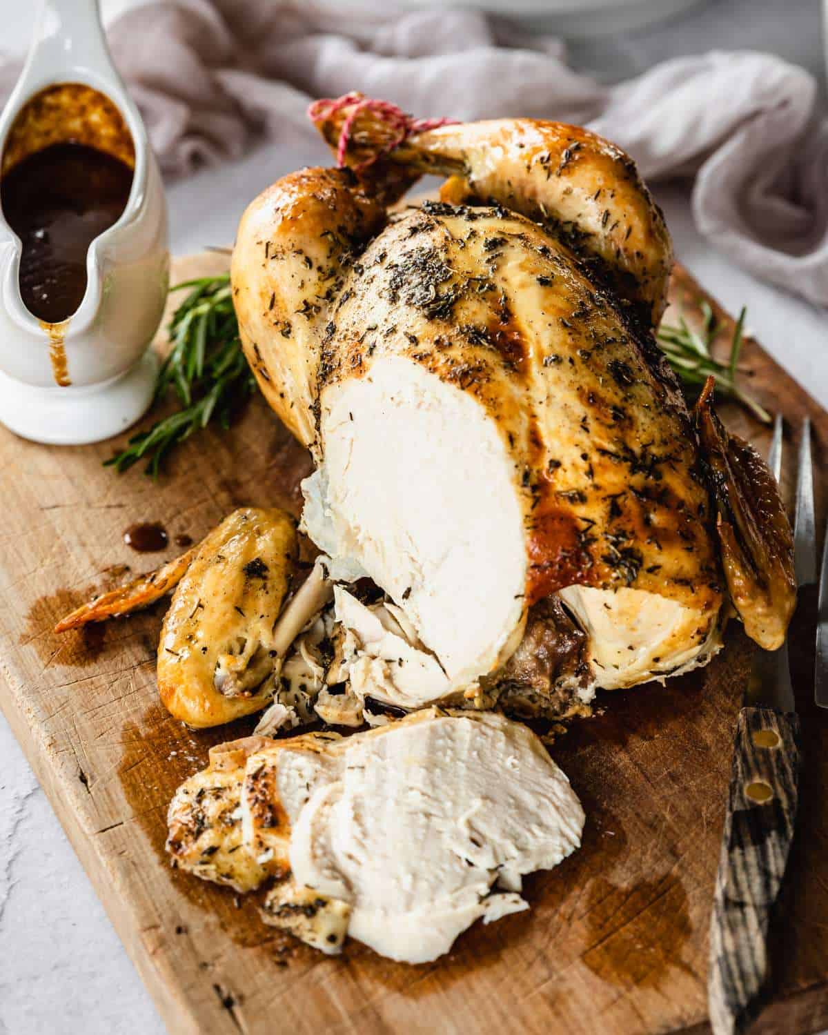 Cooked Classic Roast Chicken with a slice removed showing the cooked chicken breast on w wooden chopping board.
