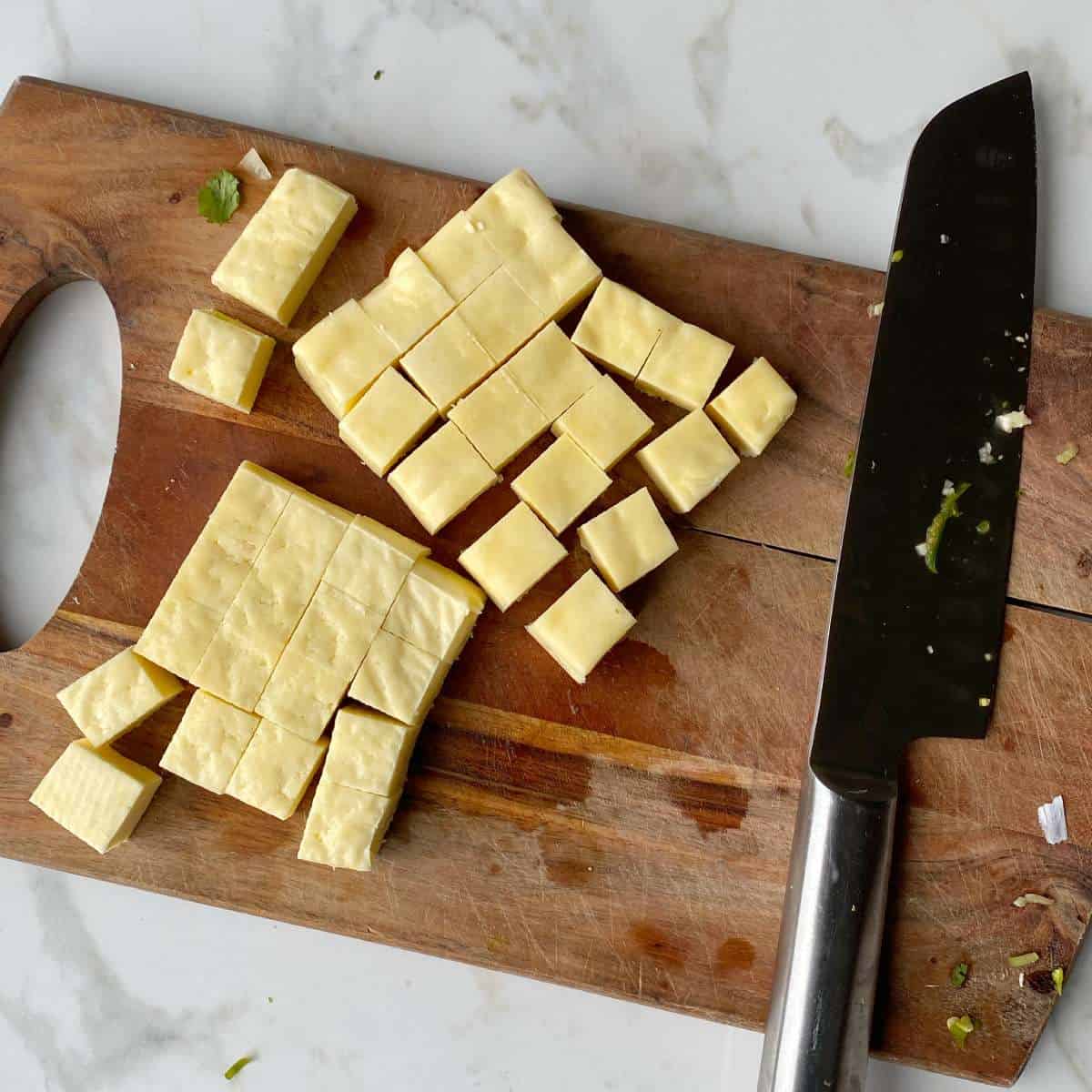 Cubed halloumi on a wooden chopping board for the paneer curry.