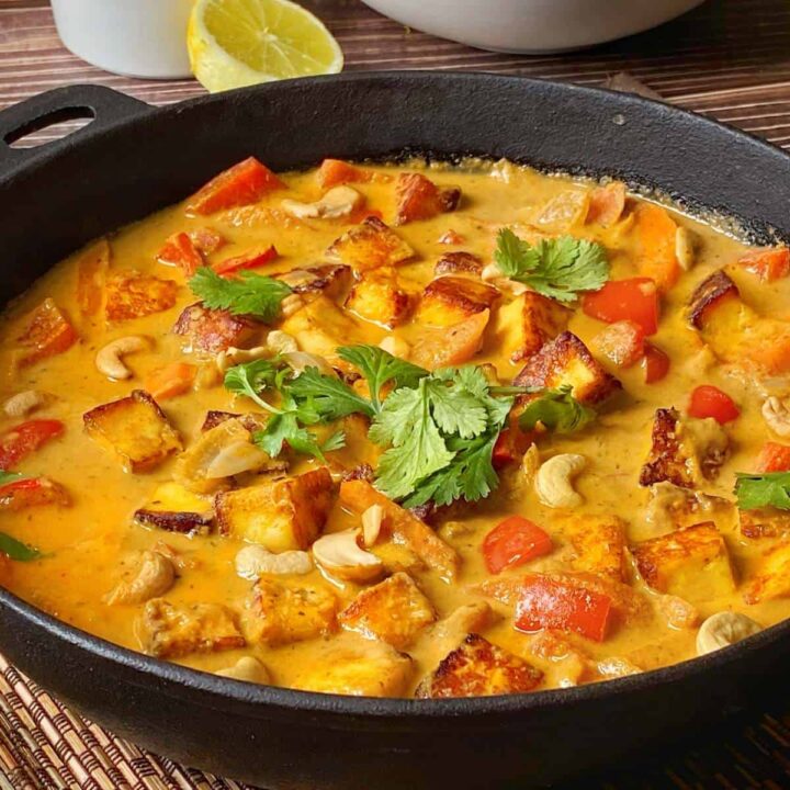 Cooked paneer curry with a garnish of coriander sitting in a frypan on a wooden chopping board.