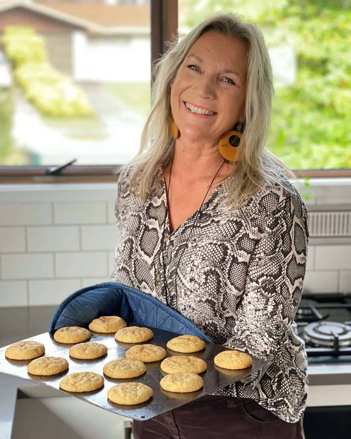 A woman holding a tray of freshly baked cookies in a kitchen.