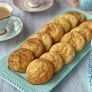 A plate of snickerdoodles on a white table with cups of tea around.