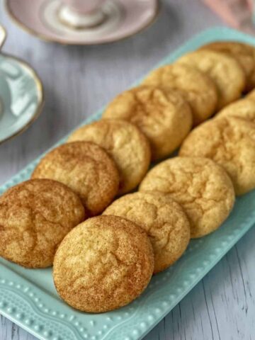 A plate of snickerdoodles on a white table with cups of tea around.