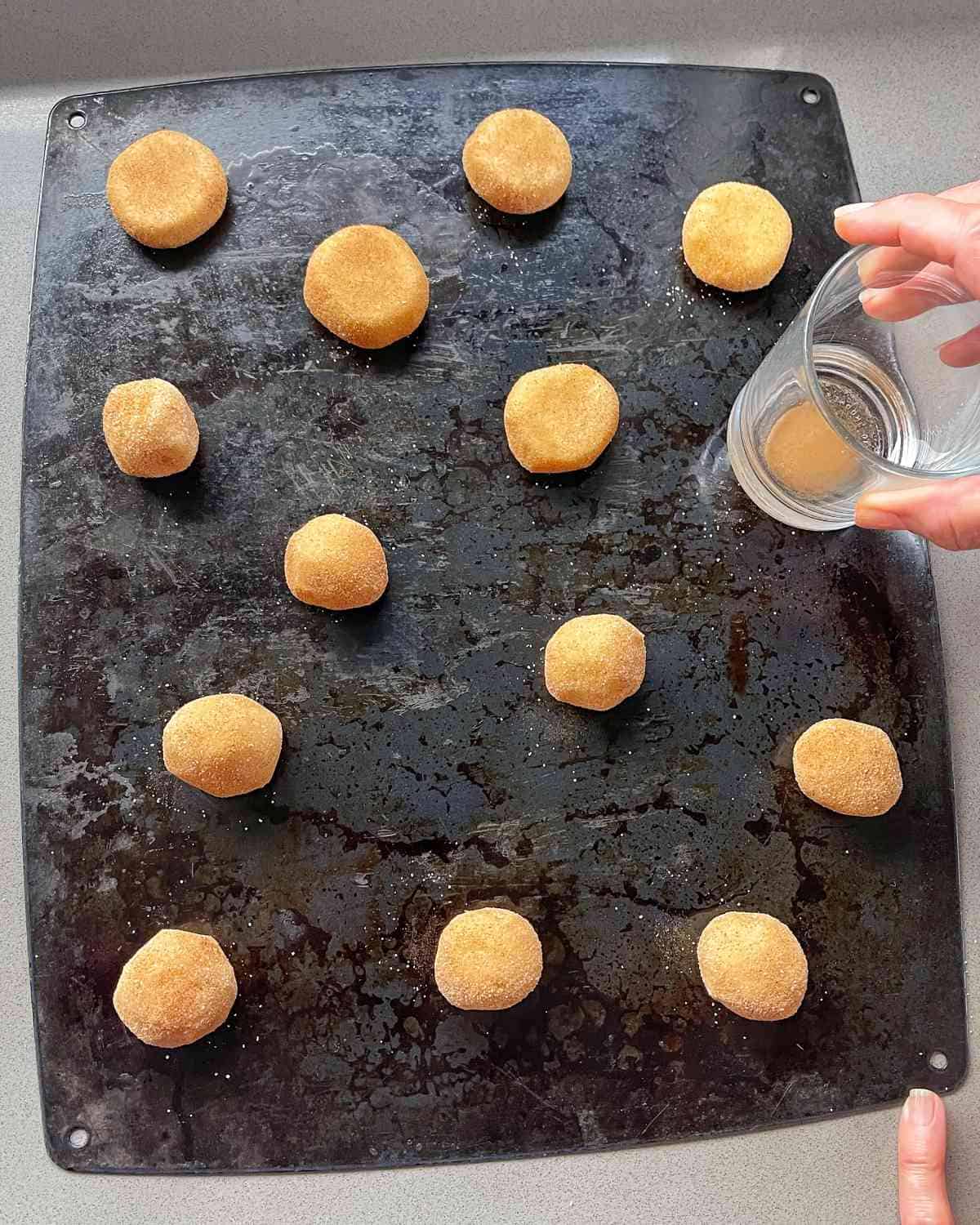Cookies being flattened on a tray using a glass cup.
