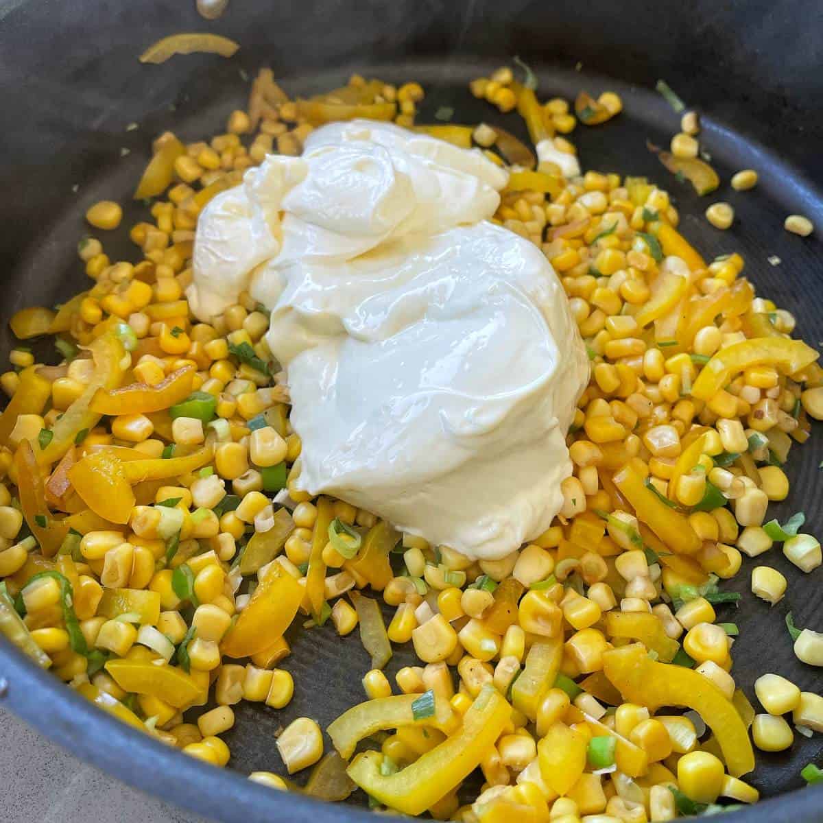 Corn kernels, yellow capsicum, sour cream and spring onions in a frying pan. 