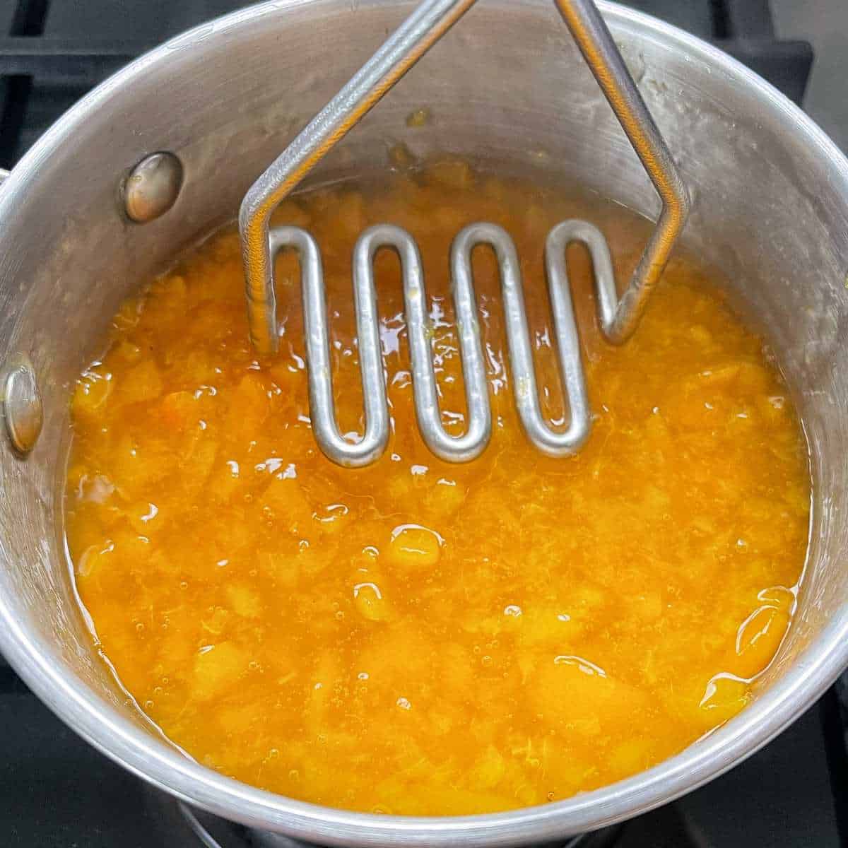 Cooked/stewed apricots being crushed with a masher for the Baked Apricot Slice.