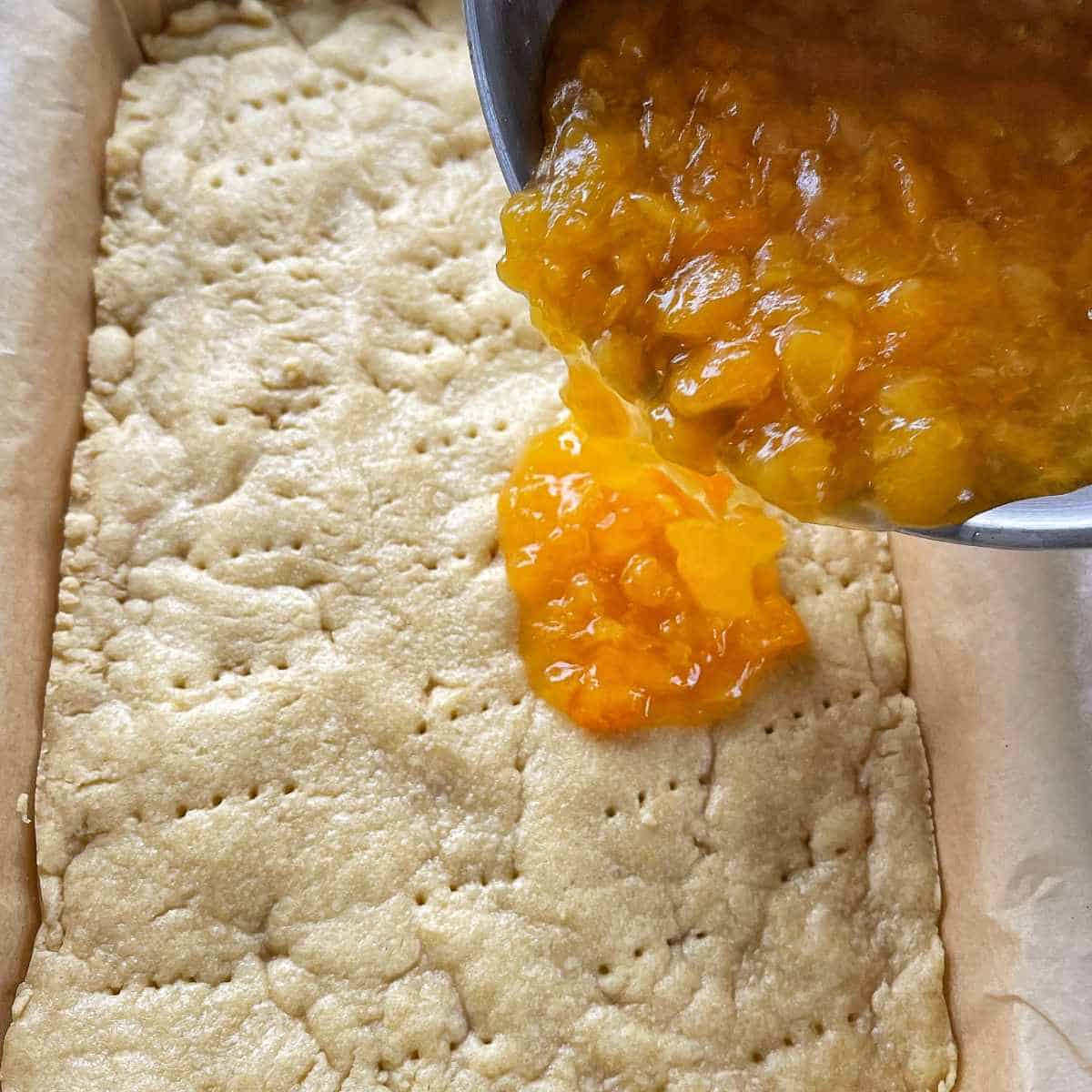 The cooked apricots being poured onto the cooked base for the baked apricot slice.