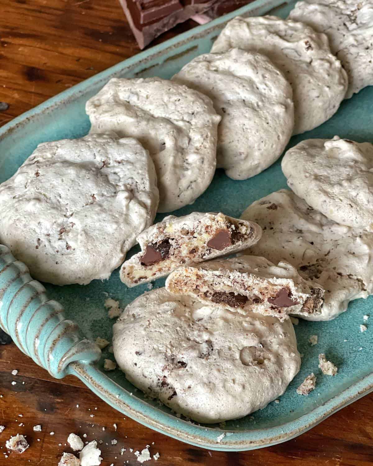 Chocolate Almond Meringue Cookies served on a long blue serving platter on a wooden table. One Cookie is snapped in half to show the meringue filling.