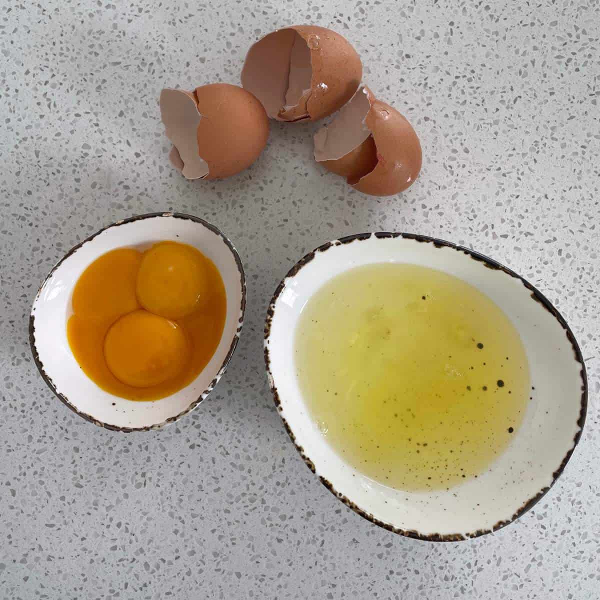 Three eggs separated into yokes and eggs whites in tow small dishes.