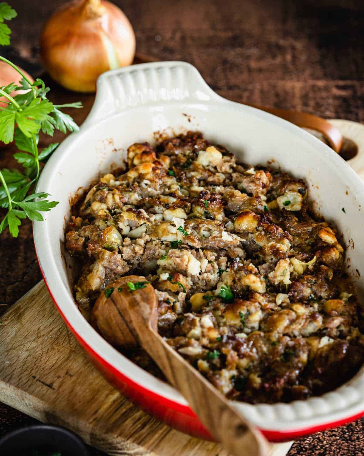 Classic Stuffing served in the oval oven dish it was cooked in on a wooden chopping board.