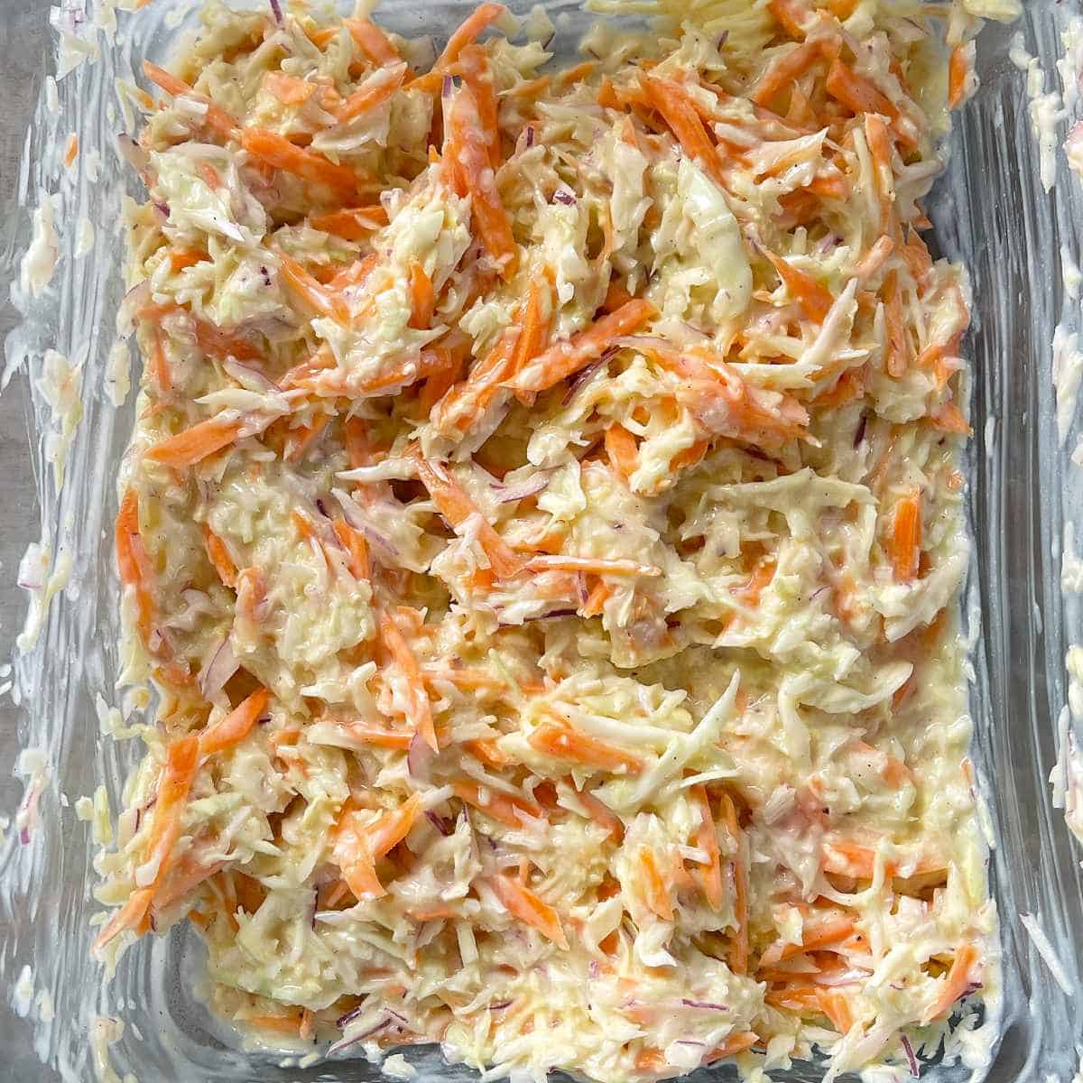 The mixed Coleslaw in a glass dish on a grey bench top.