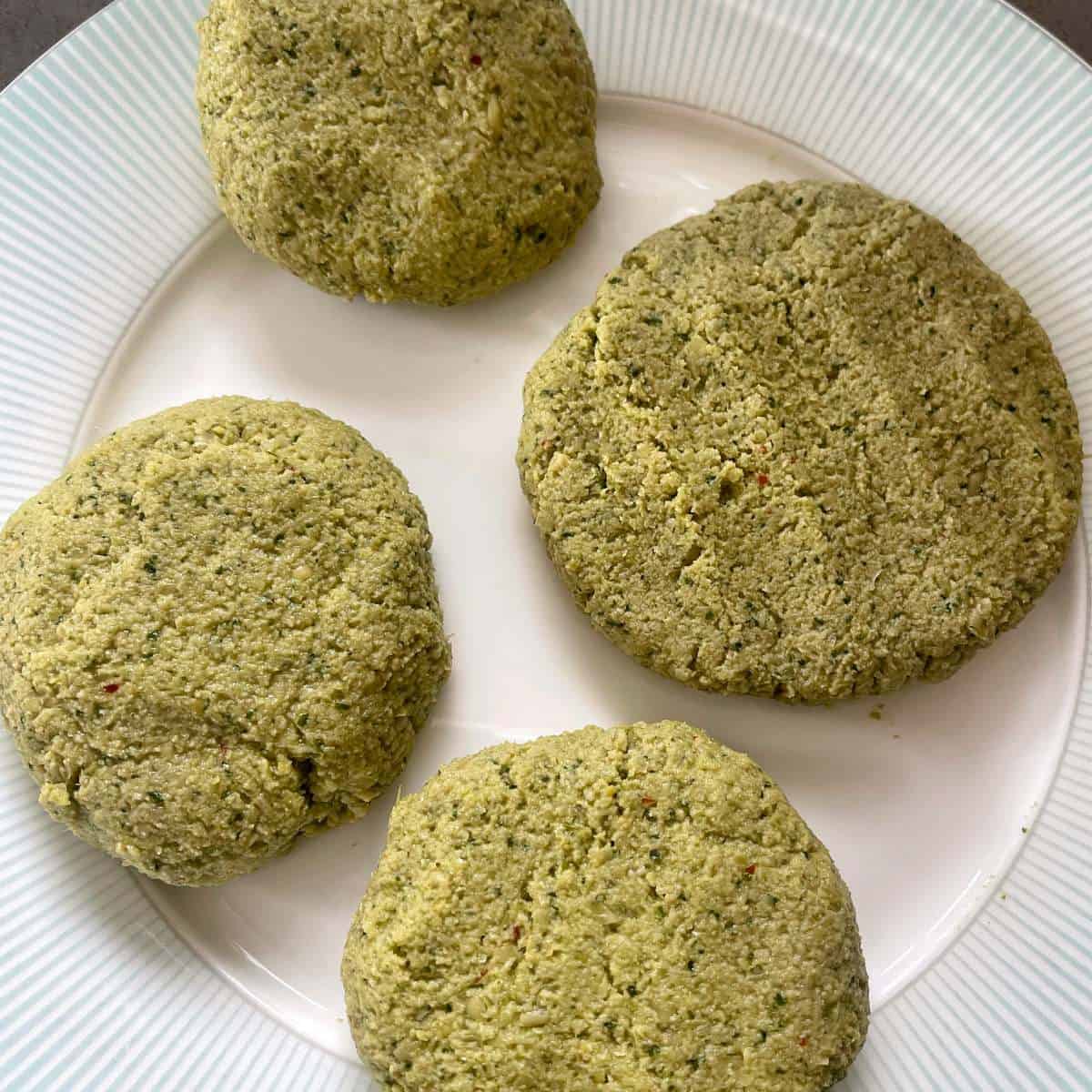Four falafel burger patties uncooked on a white plate.