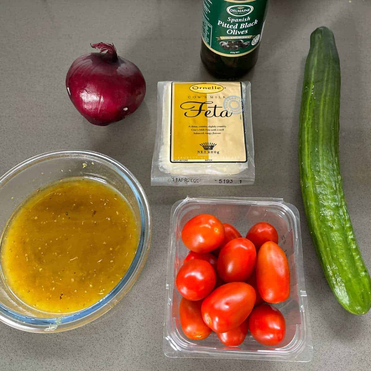 The ingredients for Greek Salad on a grey bench top.