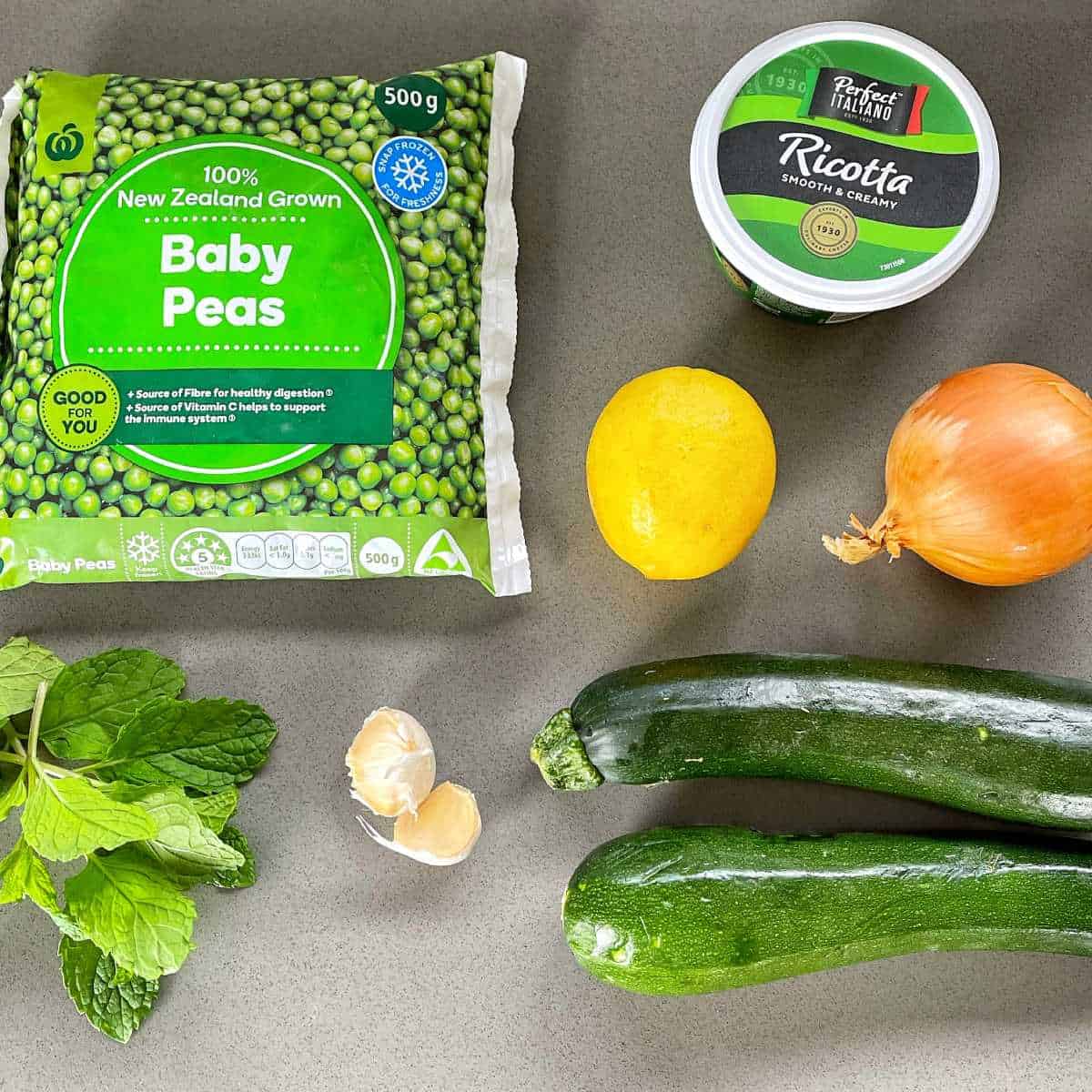 The ingredients to make pea, courgette, mint and ricotta on a grey bench top