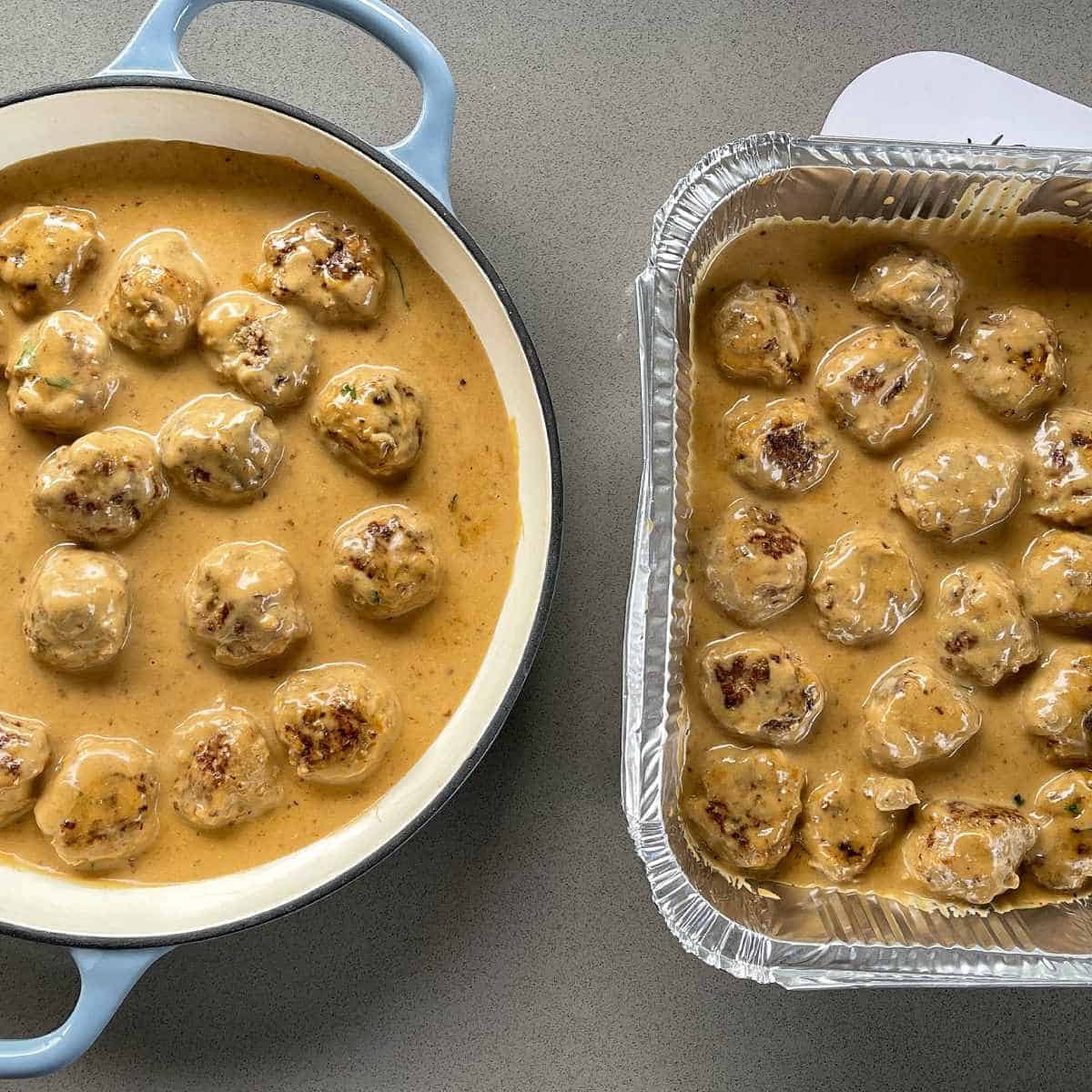 Creamy meatballs in a cast iron pan and a tinfoil tray sitting next to each other on a grey bench.