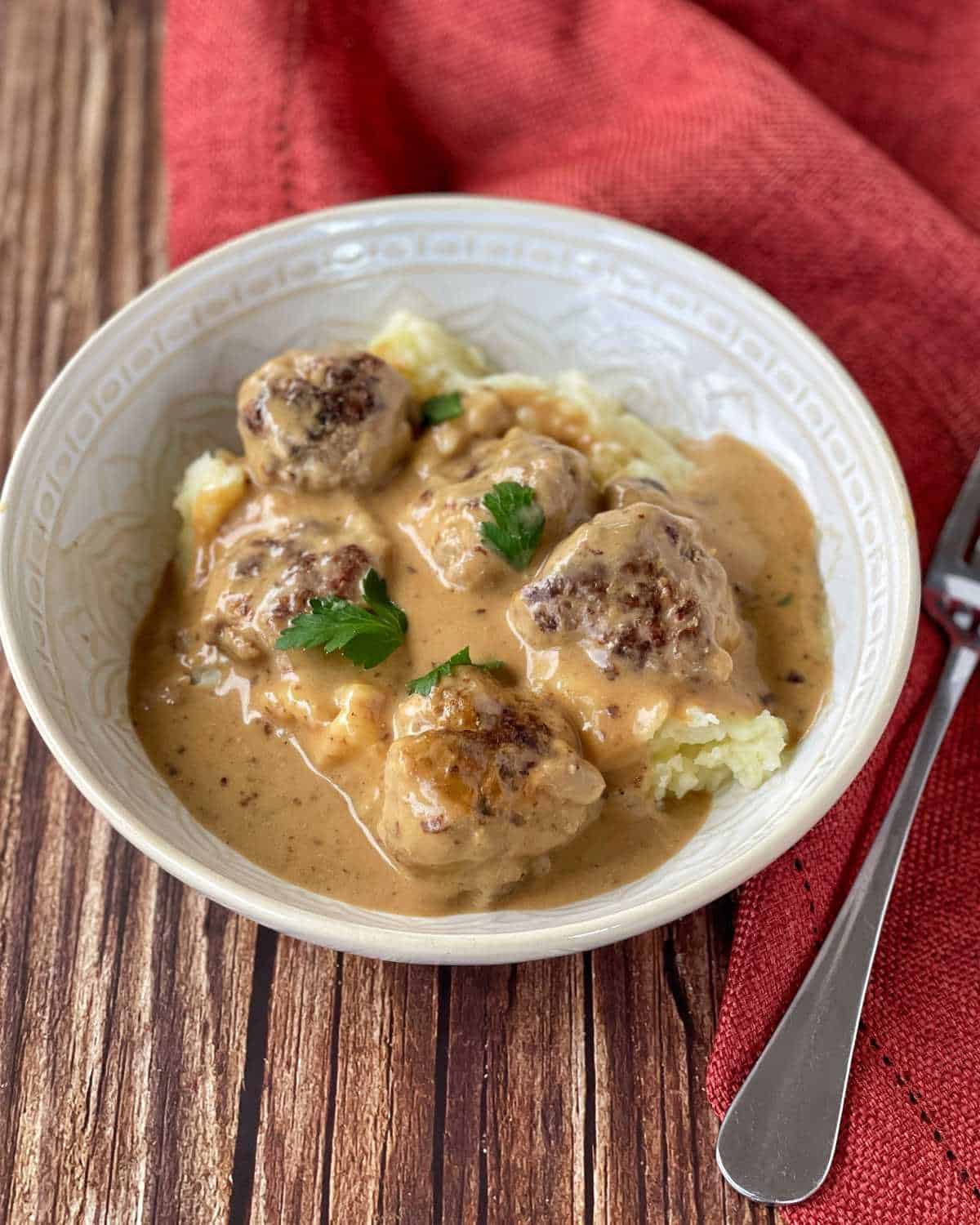 Swedish Meatballs served on mashed potatoes in a white bowl on a wooden table.