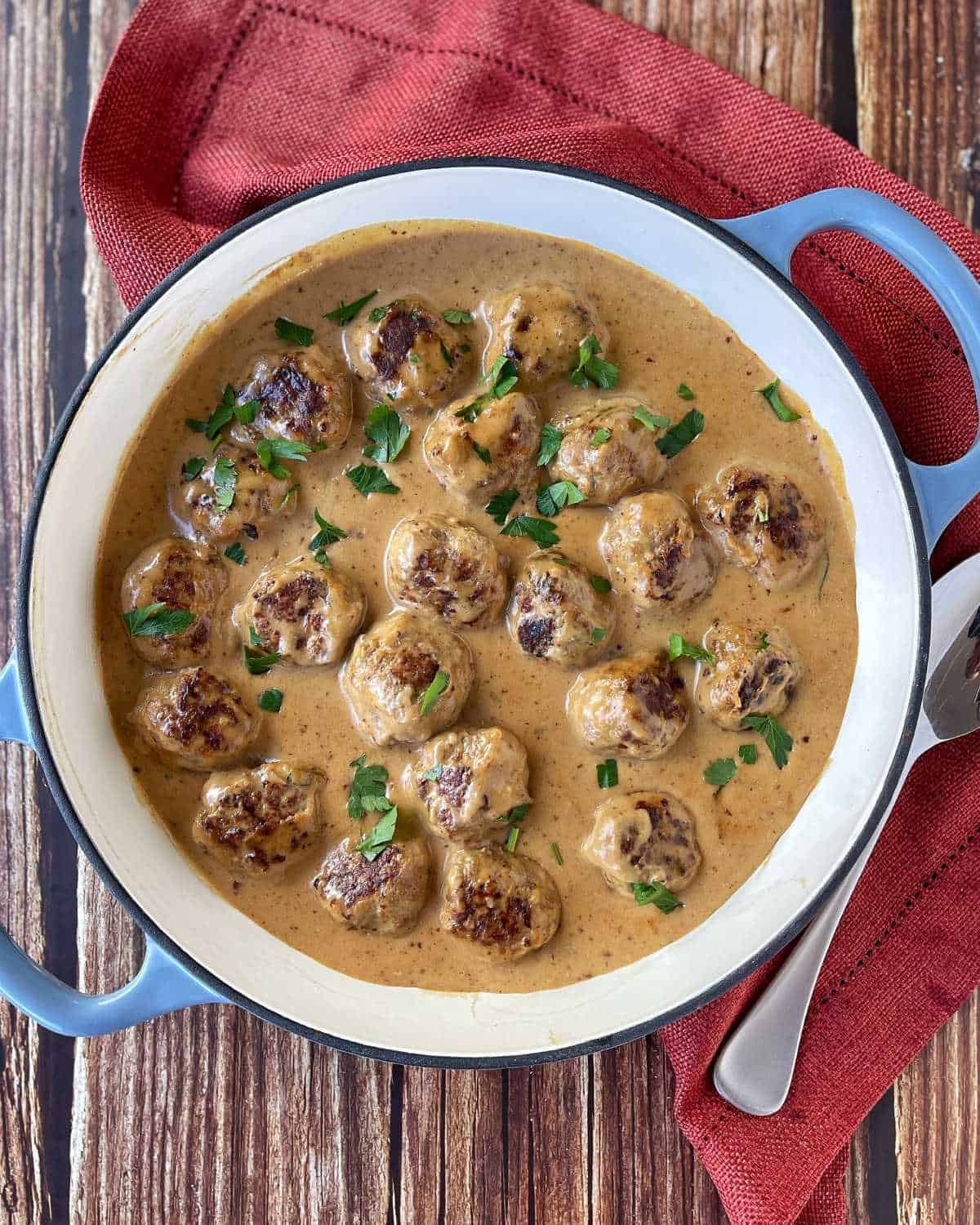 Swedish Meatballs severed in a large blue shallow bowl on a wooden table, a few sprigs of parsley to garnish.