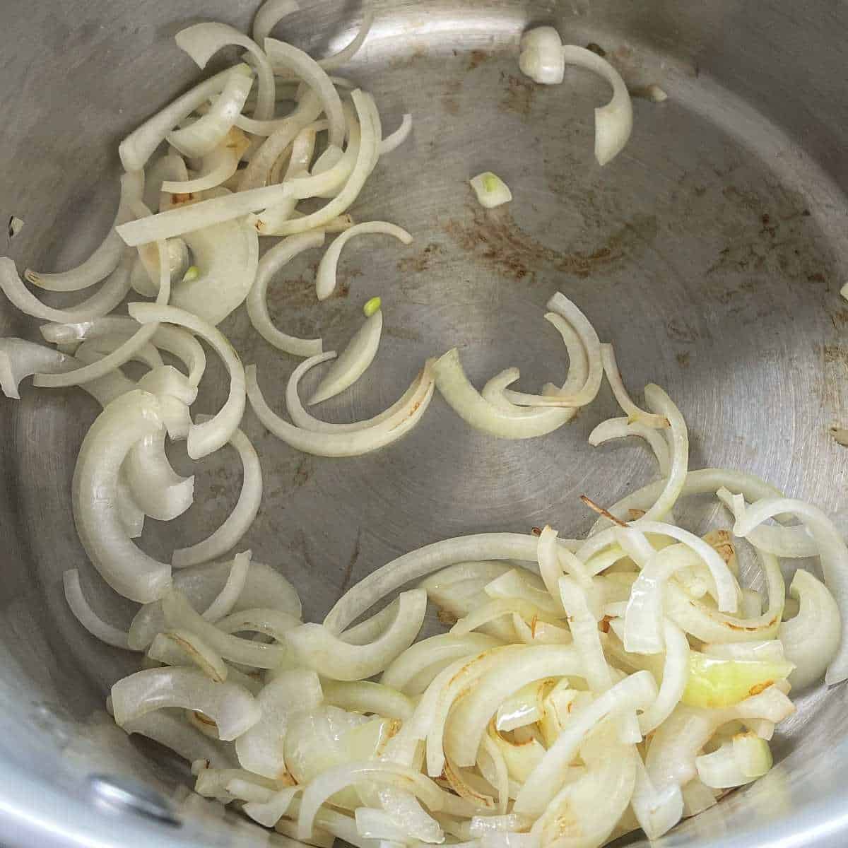 Sliced onion slowing frying in a large pot