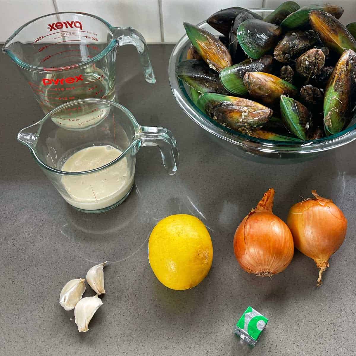 The ingredients for steamed mussels in white wine and cream sauce on a grey bench top.