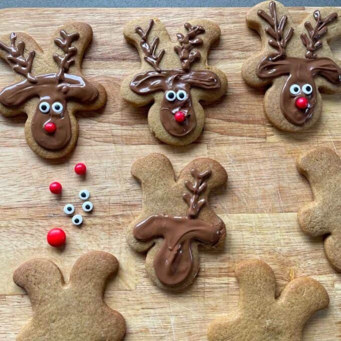 Iced gingerbread reindeer cookies on a wooden chopping board.