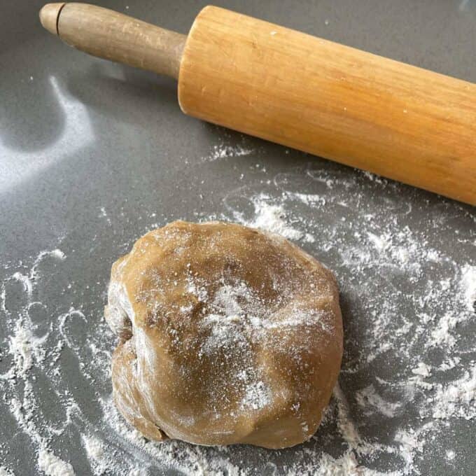 The set gingerbread cookie mixture dusted with flour on a grey bench top about to be rolled flat with a wooden rolling pin.