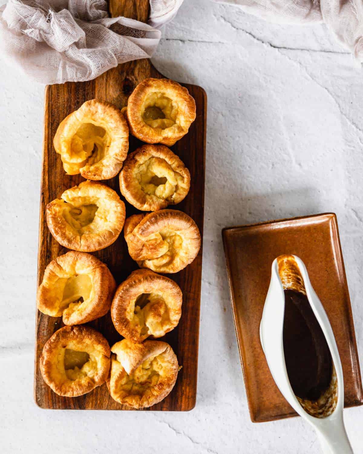 An overhead pictures of nine Yorkshire Puddings on a wooden chopping board with a rich brown gravy to the side.