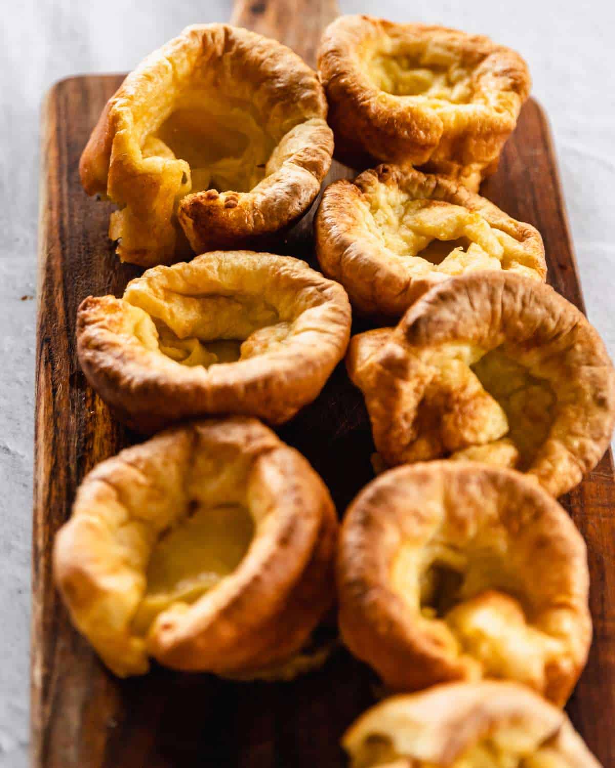 Cooked Yorkshire Puddings sitting on a wooden chopping board.