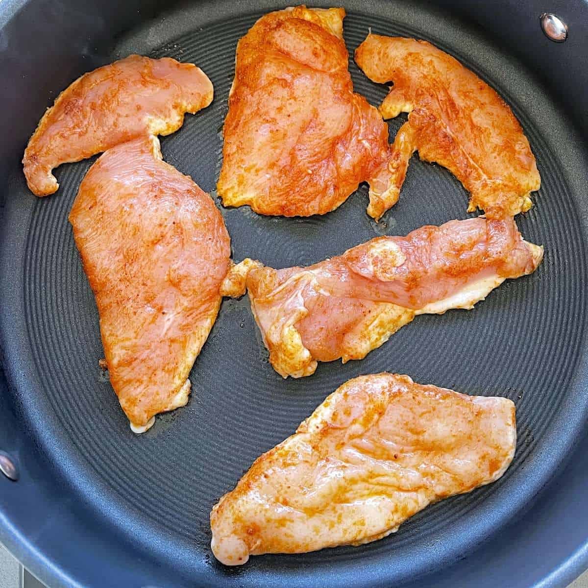 Chicken breast cooking in a frying pan. 