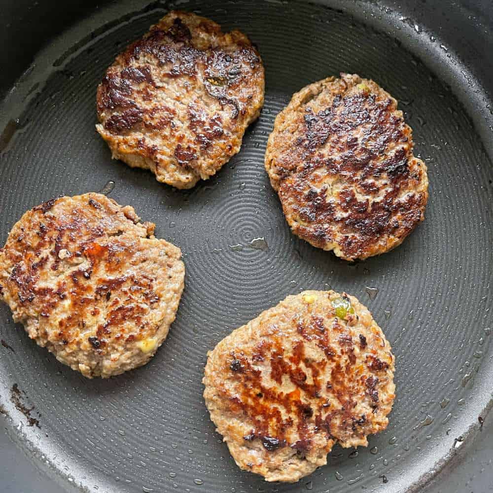 Meat patties cooking in a frying pan.