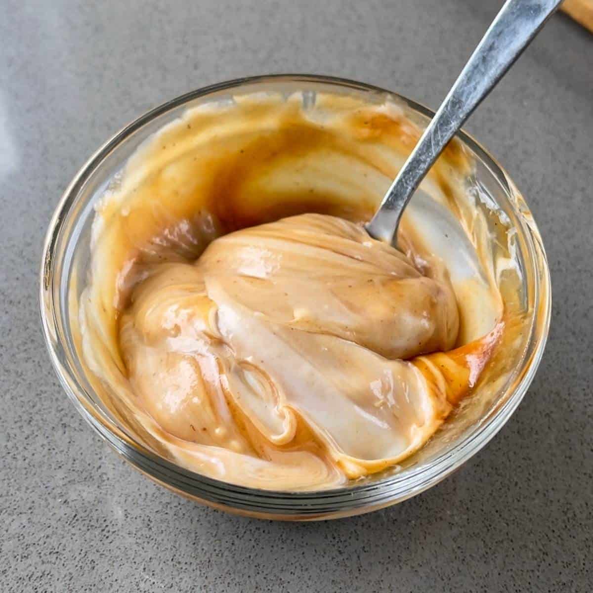 BBQ mayonnaise in a glass bowl with a tea spoon resting in it.