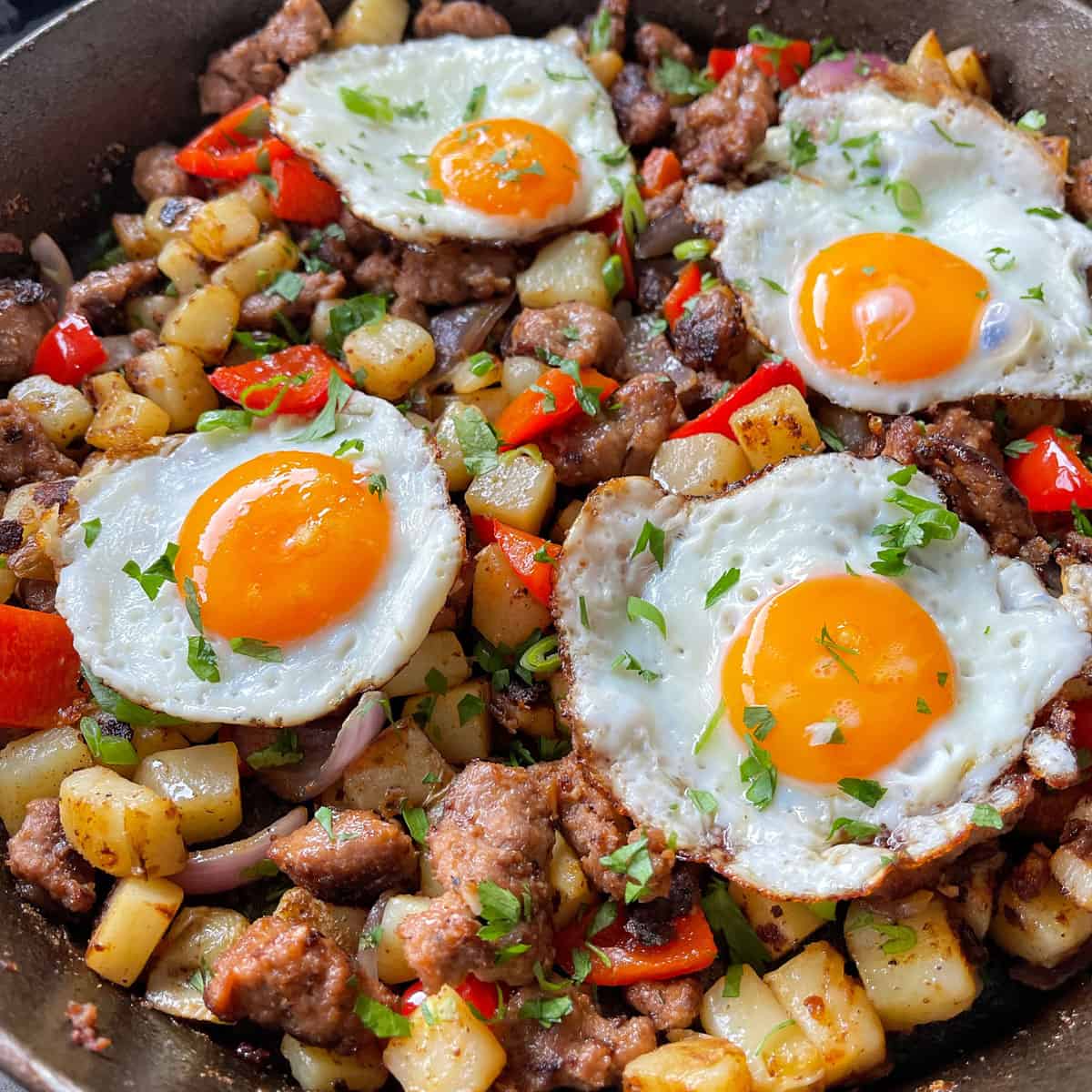 A close up of Skillet Sausage and Potatoes served with fried eggs and fresh parsley. 