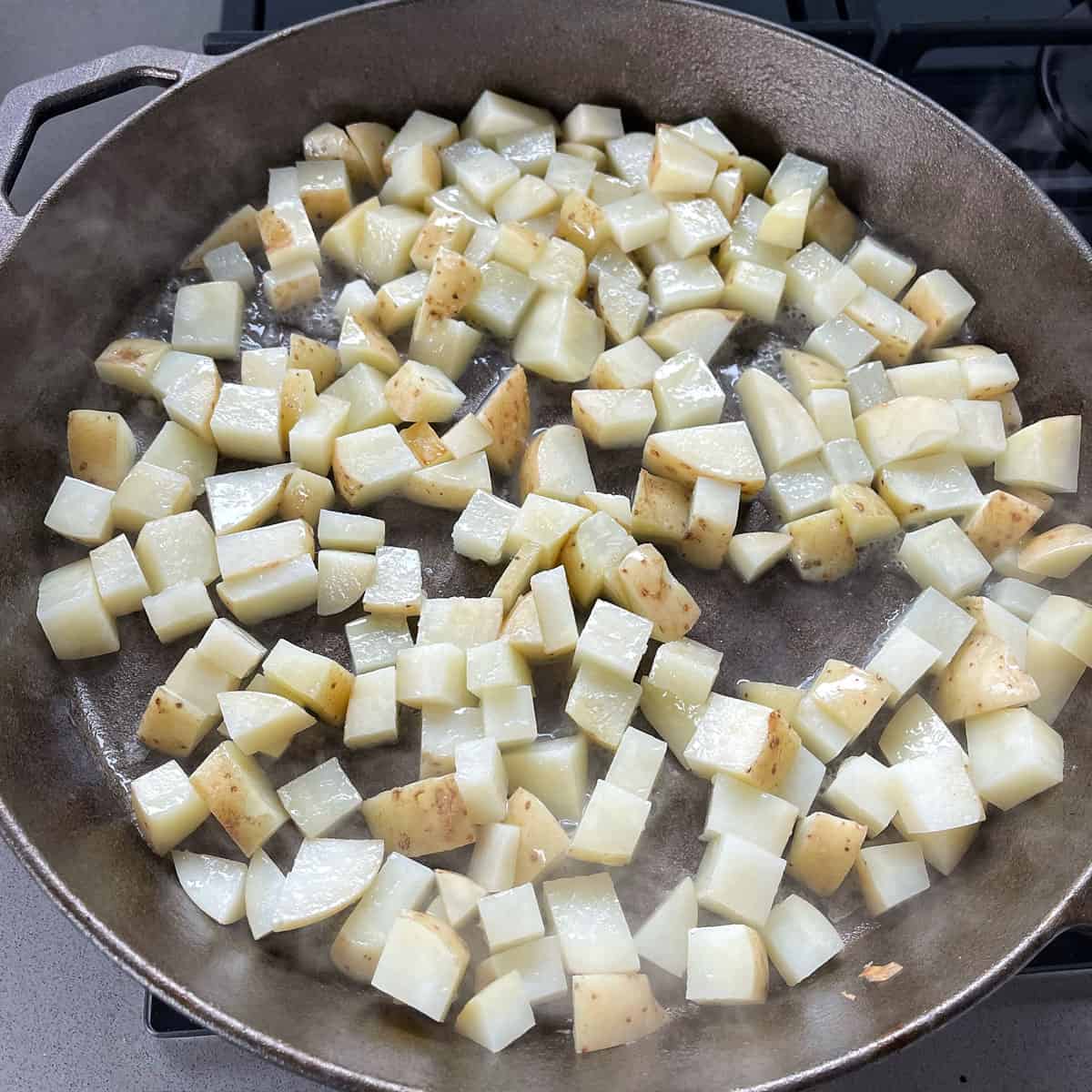 Cubed potatoes cooking in a skillet pan.