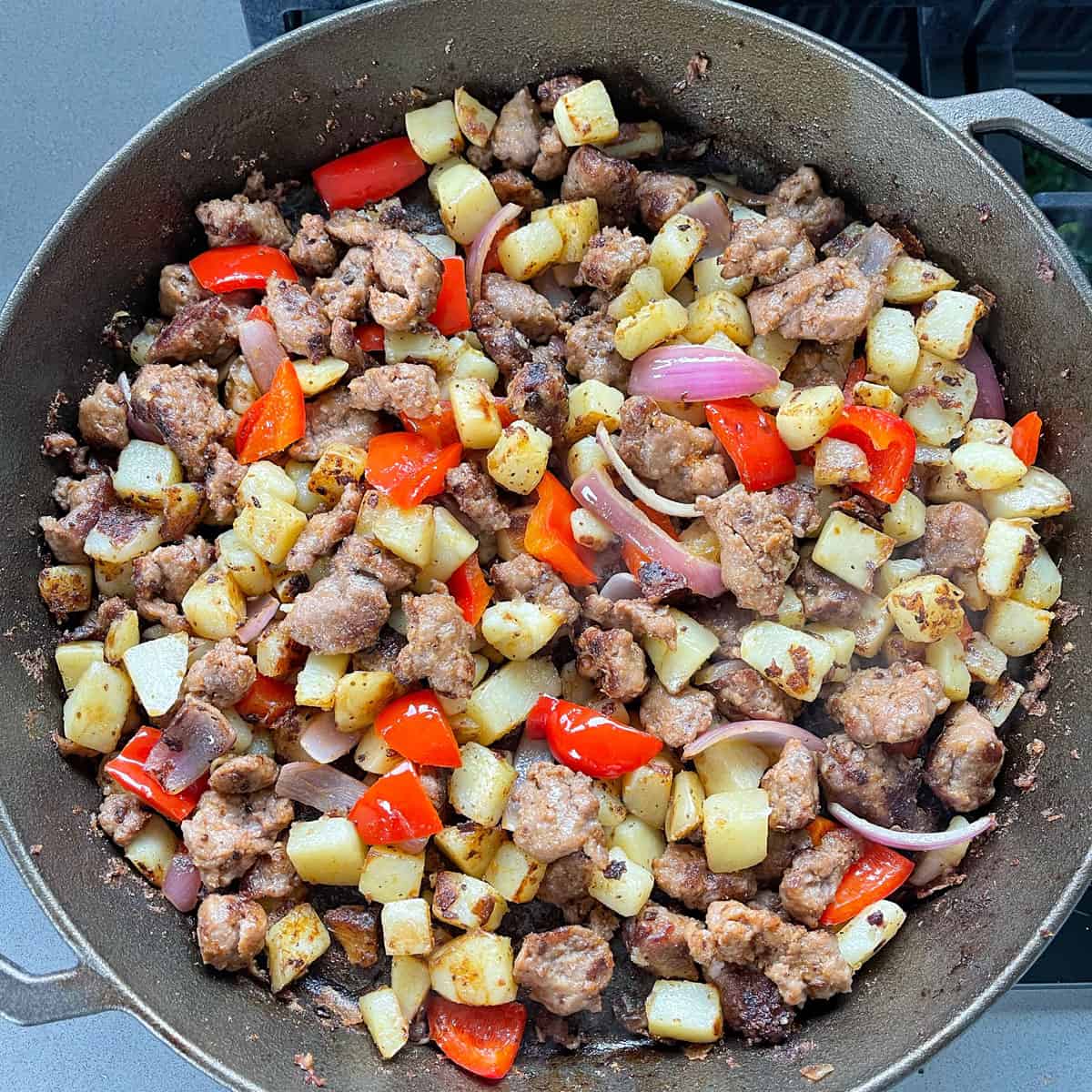 Pan fried potatoes, sausages, red onion and capsicum in a large skillet.