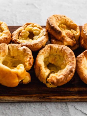 A close up of 7 Yorkshire Puddings on a wooden chopping board.