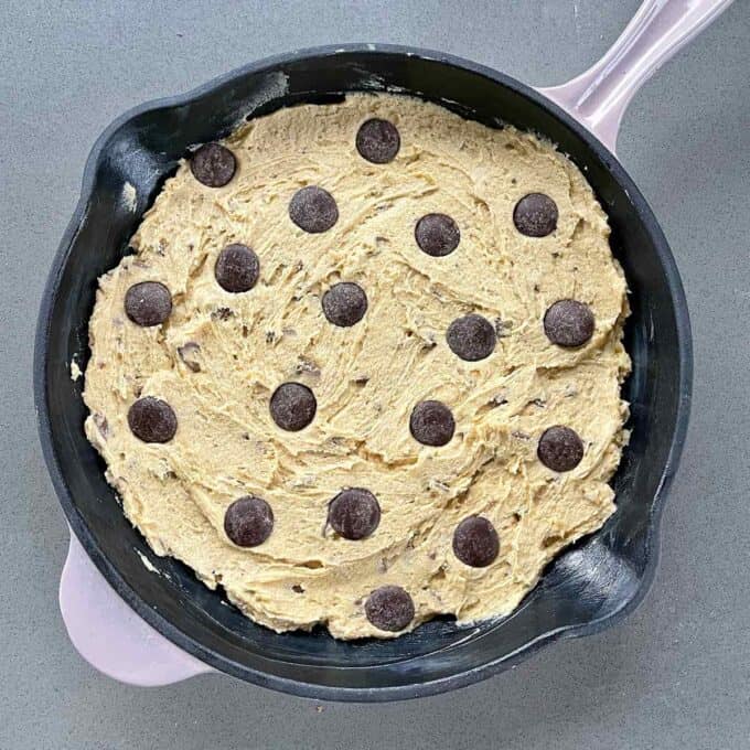 Uncooked Chocolate Chip Skillet Cookie mixture in a greased skillet pan sitting on a grey bench top.