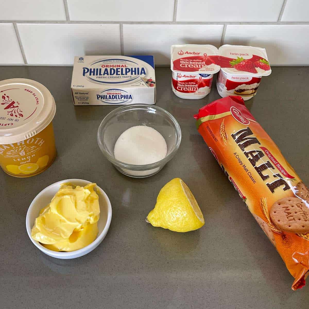 The ingredients to make lemon curd no bake cheesecake sitting on a grey bench top.