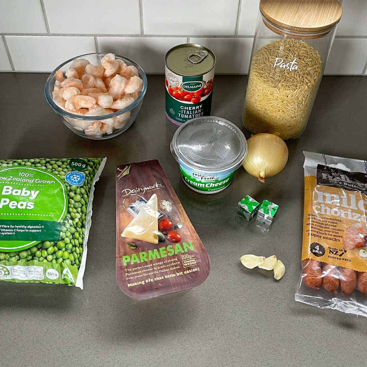 The ingredients for One-pot Chorizo, Prawn and Pea Orzo on a grey bench top.