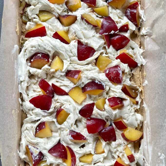 Uncooked cream cheese and plum tray bake in a lined tray about to be cooked in the oven.